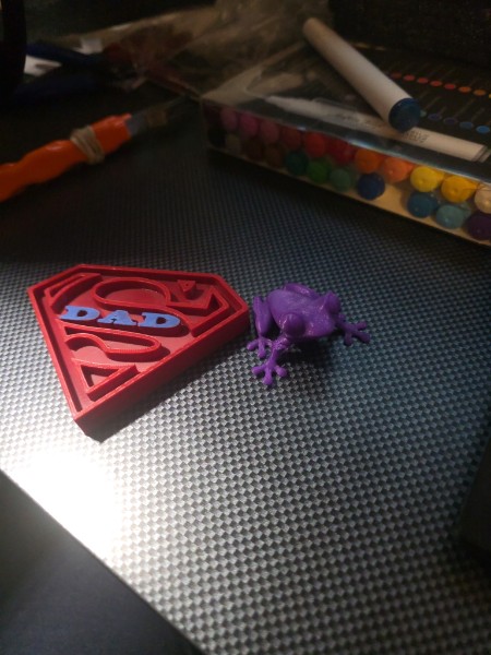 Red Superman-style shield printed with blue DAD lettering next to a purple articulated dinosaur print