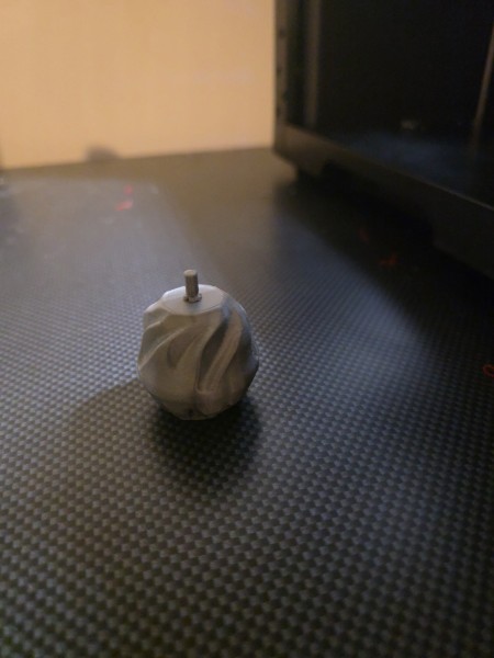 Small white and grey marbled spiral 3D print with a metal rod through the top