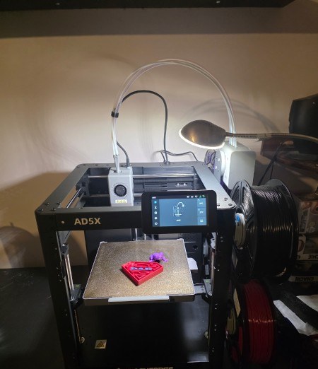 Flashforge AD5X 3D printer mid-print on the heated build plate in the Plouffe 3D Prints workshop